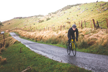 Obraz premium Young caucasian cyclist man climbing a hill in a foggy mountain.
