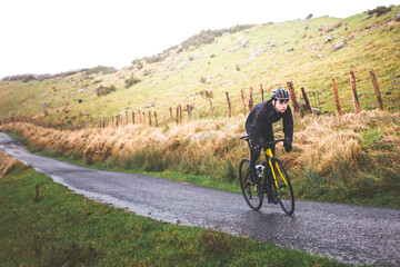 Fototapeta premium Young caucasian cyclist man climbing a hill in a foggy mountain.