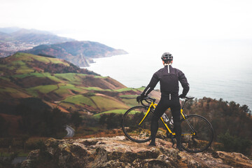Young caucasian cyclist man at the top of the mountain looking to the sea.