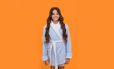 Happy girl child smiling in blue towelling bathrobe orange background, homewear