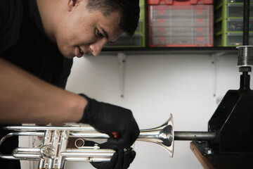 Latin male instrument repairer disassembling a trumpet in his repair shop