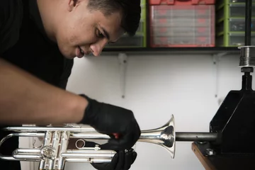 Fotobehang Muziekwinkel Latin male instrument repairer disassembling a trumpet in his repair shop