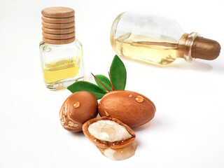 Three argan nuts with green leaves glass bottles on isolated white background. Chopped argan nut with a drop of oil. Whole and half Moroccan Argania Spinosa seeds for the production of oil
