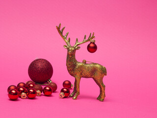 Obraz premium Xmas composition in minimal style - golden deer head with christmas bauble hanging on horns on pink background with New Year ball