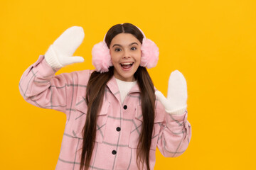 amazed child in winter mittens and earmuffs on yellow background, winter
