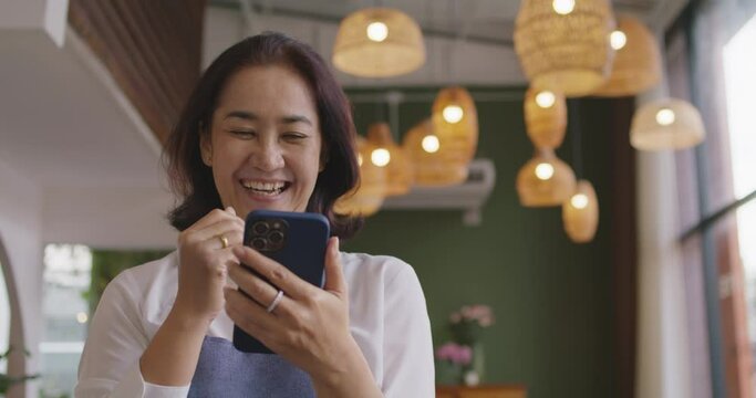 Asia mature adult woman people wear apron small cafe receive e-mail text good news SME lending service solution win seller store in social media app. Shock smile laugh face in sale order reopen shop.