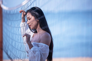 A caucasian woman posing hold hand on a volleyball net on tropical beach