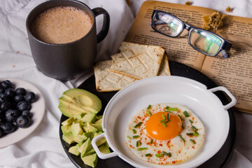 Healthy homemade breakfast with chocolate, fried egg with chives, toast, avocado and blueberries.