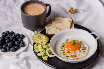 Healthy homemade breakfast with chocolate, fried egg with chives, toast, avocado and blueberries.