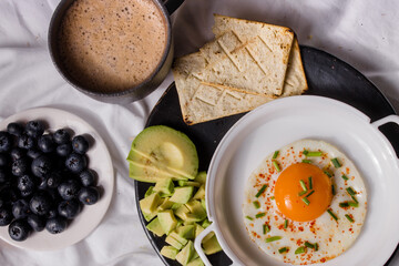 Healthy homemade breakfast with chocolate, fried egg with chives, toast, avocado and blueberries.