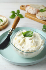 Tasty cream cheese with basil and knife on white wooden table