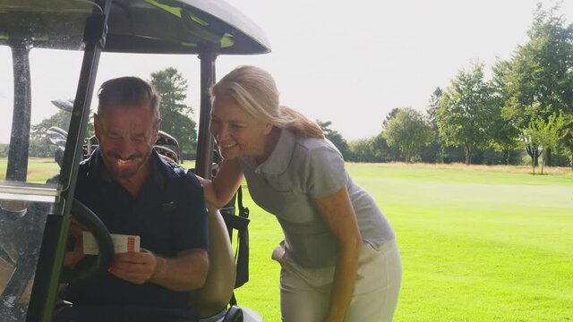 Mature couple playing round of golf sitting in buggy checking score card together - shot in slow motion