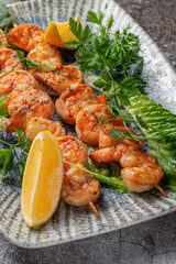 Grilled king prawns with lemon and herbs on a plate against a gray stone table, fish kebab