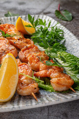 Grilled king prawns with lemon and herbs on a plate against a gray stone table, fish kebab