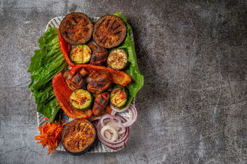 Grilled vegetables with onions and herbs in a plate against a gray stone table, vegan kebab
