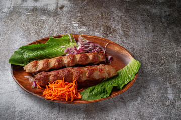 Meat kebab and barbecue with onions, Korean carrots and green salad in a plate against the background of a gray stone table 