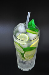 Tall glass of refreshing Mojito with ice, mint and lime slices on a black background.