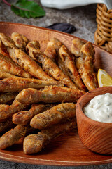 An fish appetizer in a restaurant, fried sprat on a wooden plate with lemon and cream sauce against a gray stone table 