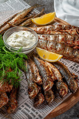 An fish appetizer in a restaurant, fried sprat on a wooden plate with lemon and cream sauce against a gray stone table 