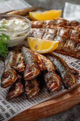 An fish appetizer in a restaurant, fried sprat on a wooden plate with lemon and cream sauce against a gray stone table 