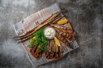 An fish appetizer in a restaurant, fried sprat on a wooden plate with lemon and cream sauce against a gray stone table  - obrazy, fototapety, plakaty