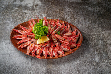 An appetizer in a restaurant, boiled shrimp on a wooden plate with lemon and herbs against a gray stone table 