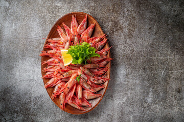 An appetizer in a restaurant, boiled shrimp on a wooden plate with lemon and herbs against a gray stone table 