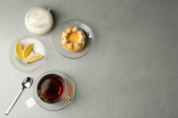 Flat lay composition with tea bag in ceramic cup of hot water and dessert on grey table. Space for text