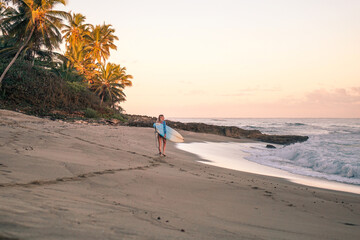 Portrait of blond surfer girl with white surf board in blue ocean pictured from the water in Encuentro beach