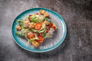 Healthy salad with fried shrimp, greens and croutons in a plate against a gray stone table. A healthy breakfast in a restaurant