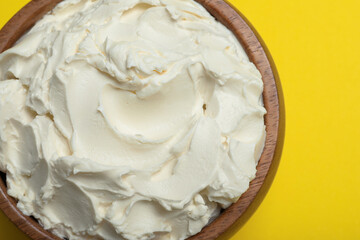 Bowl of tasty cream cheese on yellow background, top view