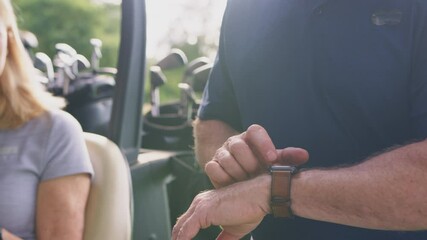 Close up of mature man checking smart watch as couple sit in buggy and play a round of golf together - shot in slow motion - Powered by Adobe