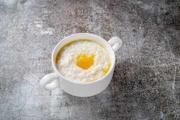 Rice porridge with butter in a white cup against a gray stone table. A healthy breakfast in a restaurant .