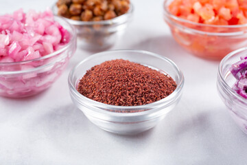A view of a glass cup of ground sumac, among a variety of other chopped ingredients.
