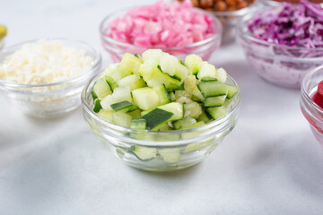 A view of a glass cup of chopped cucumbers, among a variety of other chopped ingredients.
