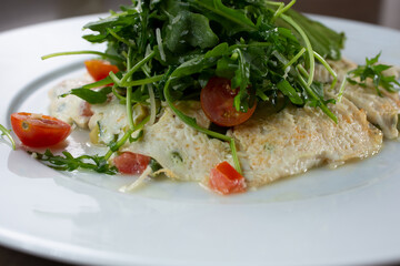 A closeup view of a white egg omelet, with an arugula salad.
