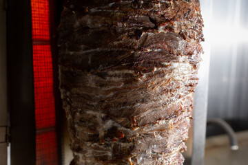 A closeup view of a rotisserie spit machine heating up beef shawarma.