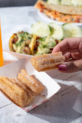 A view of a hand holding a churro next to several street food entrees.