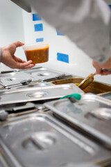 A view of an employee scooping prepared ingredients from metal pans on a steamer table, seen at a local restaurant.