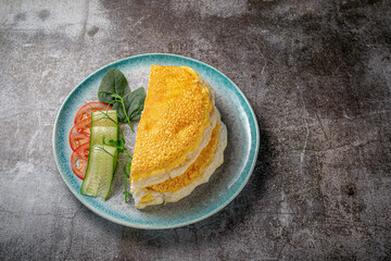 Omelet with fresh herbs and tomatoes in a blue plate with spices against a gray stone table .