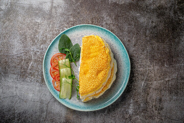 Omelet with fresh herbs and tomatoes in a blue plate with spices against a gray stone table .