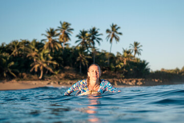 Portrait of blond surfer girl on white surf board in blue ocean pictured from the water in...