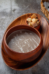 Mashed mushroom soup in a wooden bowl on a tray with bread crumbs against a gray stone table .