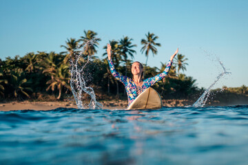 Portrait of blond surfer girl on white surf board in blue ocean pictured from the water in...