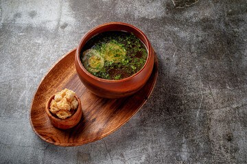 Chicken soup with boiled egg sprinkled with dill and parsley greens in a wooden bowl with bread crumbs stands isolated on a stone table, Flatlay