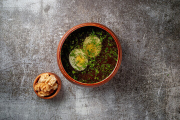 Chicken soup with boiled egg sprinkled with dill and parsley greens in a wooden bowl with bread crumbs stands isolated on a stone table, Flatlay