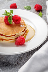 A delicious breakfast. Sweet fried raspberry and mint pancakes in a white plate with sour cream on a gray stone table with a napkin and cutlery