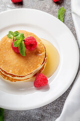 A delicious breakfast. Sweet fried raspberry and mint pancakes in a white plate with sour cream on a gray stone table with a napkin and cutlery