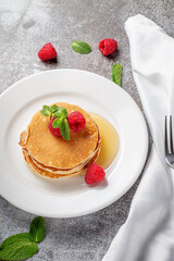 A delicious breakfast. Sweet fried raspberry and mint pancakes in a white plate with sour cream on a gray stone table with a napkin and cutlery