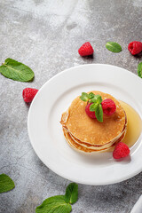 A delicious breakfast. Sweet fried raspberry and mint pancakes in a white plate with sour cream on a gray stone table with a napkin and cutlery